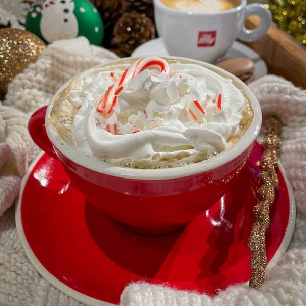 A festive iCafe de Paris peppermint mocha with whipped cream and candy canes in a red mug.