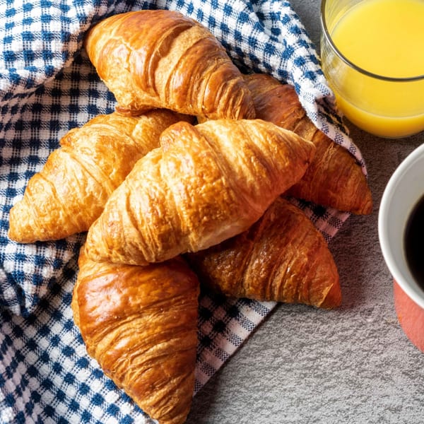 Golden croissants on a blue and white checkered cloth with orange juice and coffee.
