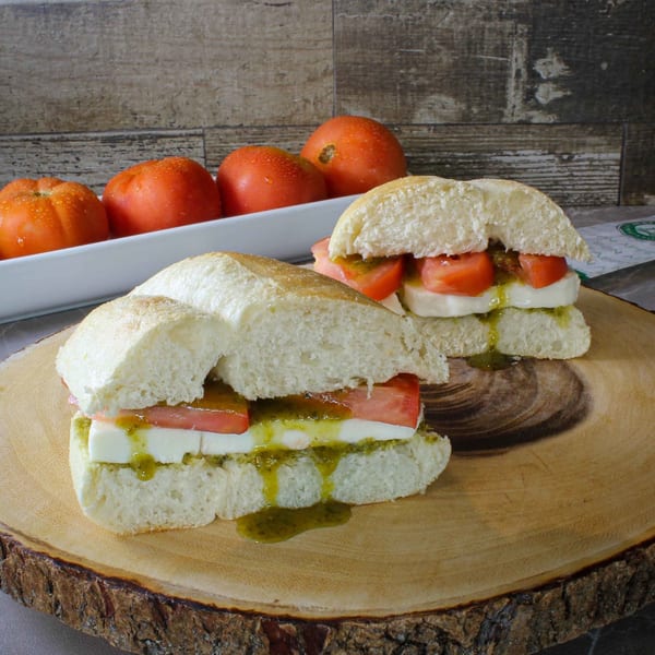 Two iCafe de Paris caprese sandwiches with fresh tomatoes, mozzarella, and pesto on a wooden board.