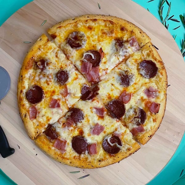A sliced pepperoni and ham pizza with melted cheese on a wooden board with a pizza cutter.