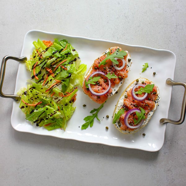 Two salmon and cream cheese bruschettas with red onion, capers, and arugula, alongside a green salad.