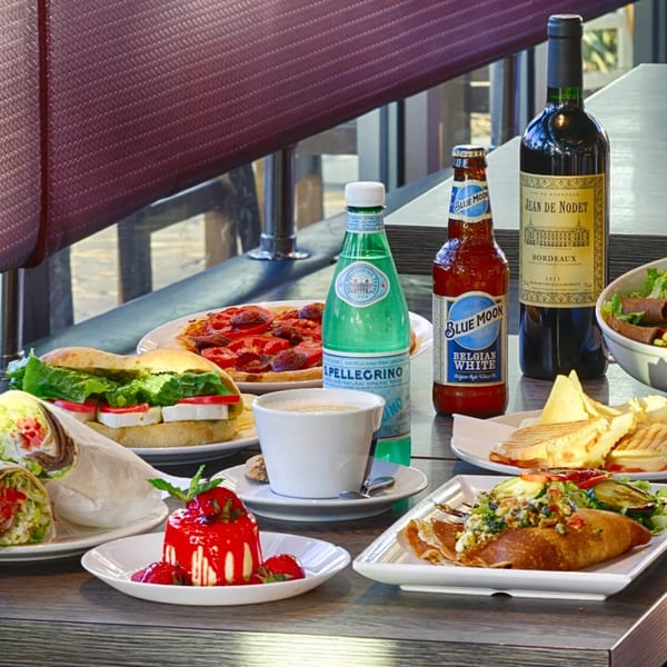 A cafe table laden with sandwiches, crepes, pastries, coffee, wine, and sparkling water.